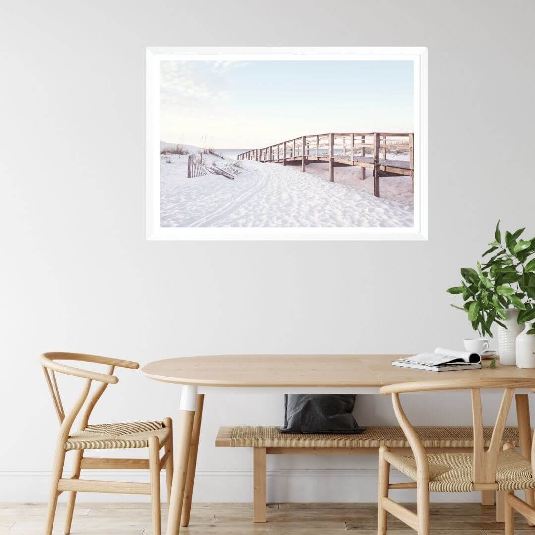 A wall art photo print of a beachside boardwalk with a white frame, white border on dining room wall