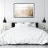 A wall art photo print of a grassy beach shore with a black frame, white border on wall above bed