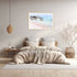 A wall art photo print of a pink beach in Greece with a tumber frame, white border on wall above bed in bedroom