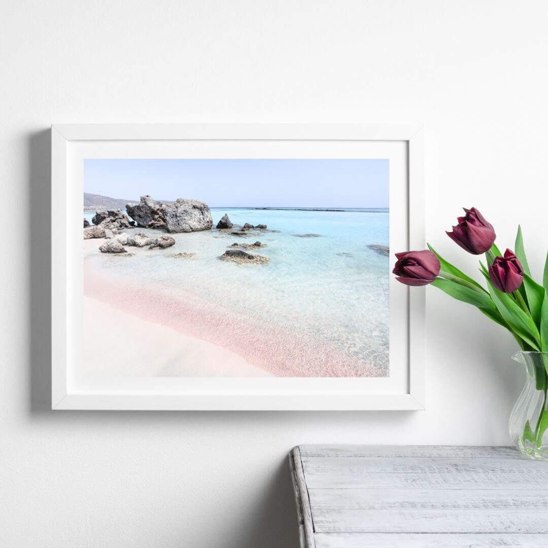 A wall art photo print of a pink beach in Greece with a white frame or unframed to style shelves and empty walls