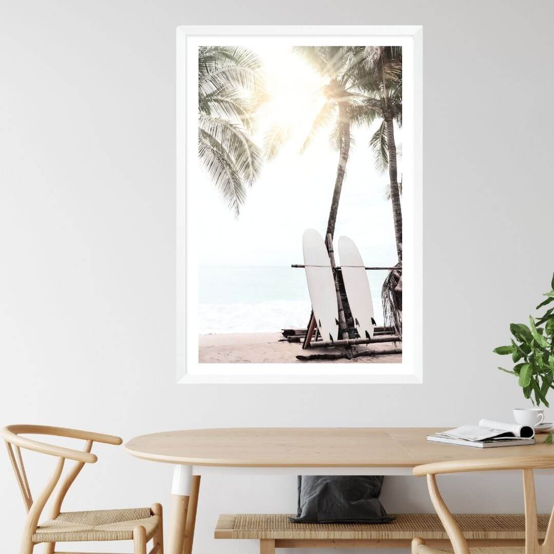 A wall art print of two white surfboards on a surfer beach in Hawaii under the palm trees with a sunset view in a dining room
